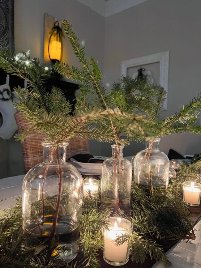 clear glass bottles with Noble Fir stems and candles as a table centerpiece