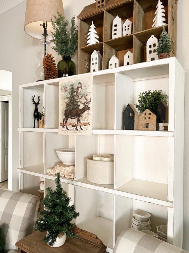 large cubby shelf with white ceramics, brown doll house and Christmas trees
