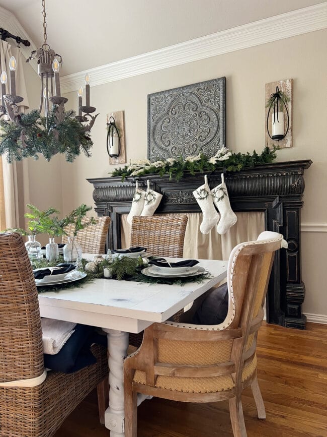 black mantel in dining room with white stockings and candles. Table with fresh greens, white plates.