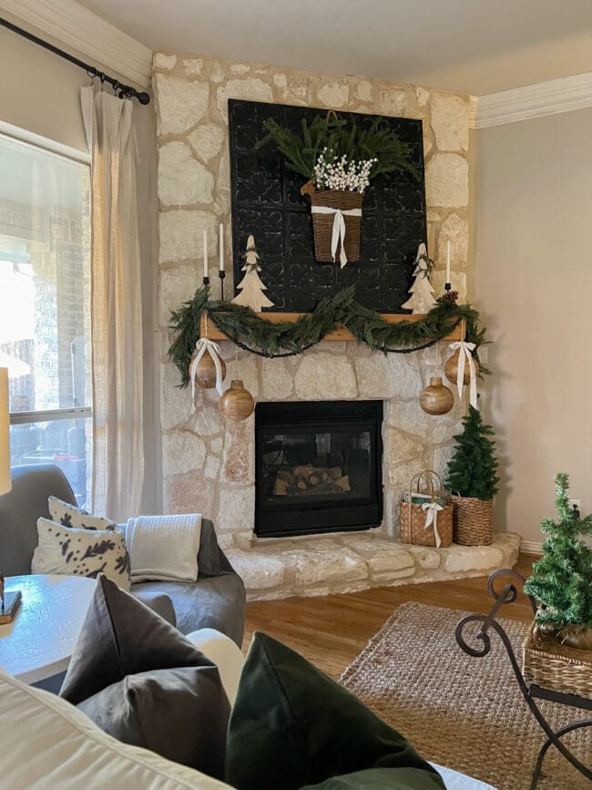 Stone Christmas mantel with green garland, small tree and large wooden bells