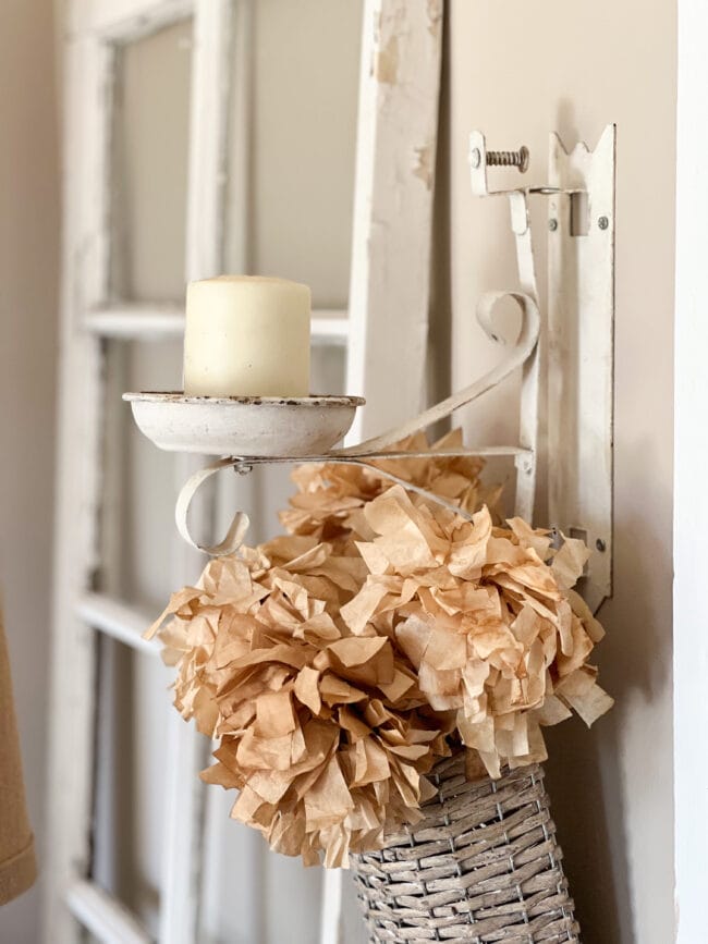 vintage piece repurposed as a candle holder hanging on wall with paper flowers underneath