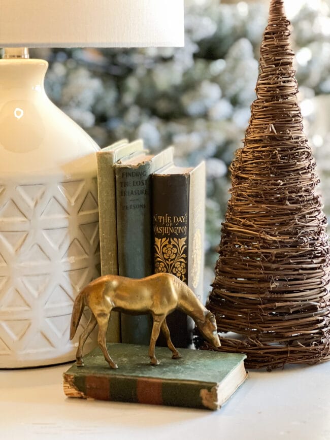 side table with white lamp, green books, brass horse and twig tree on the edge