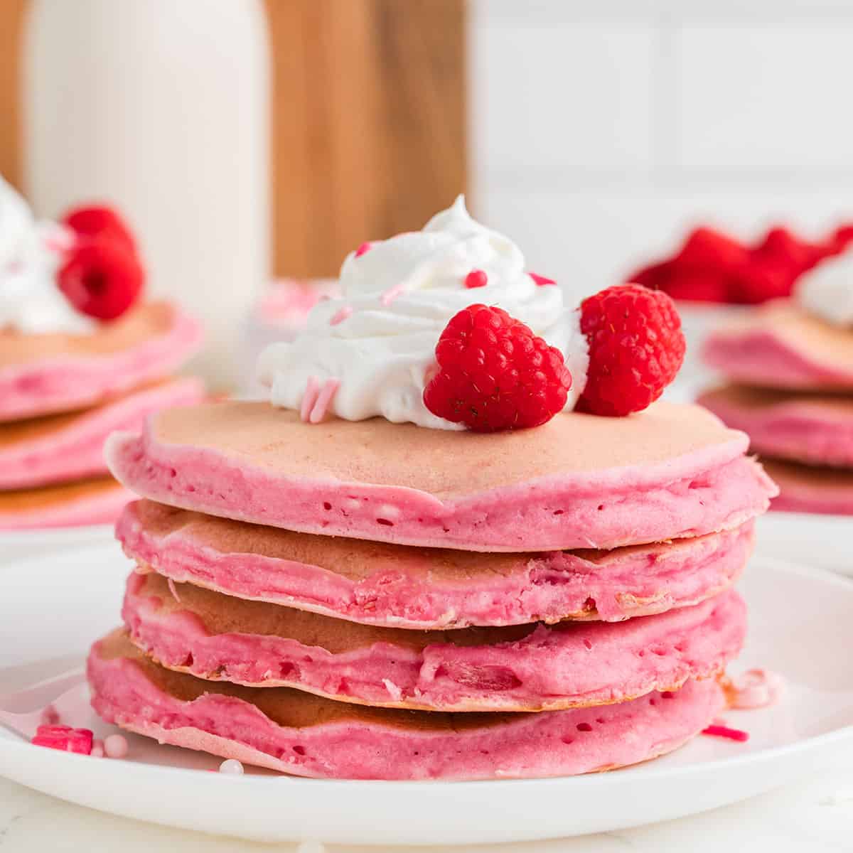 stack of pink pancakes with raspberries and whipped cream on top