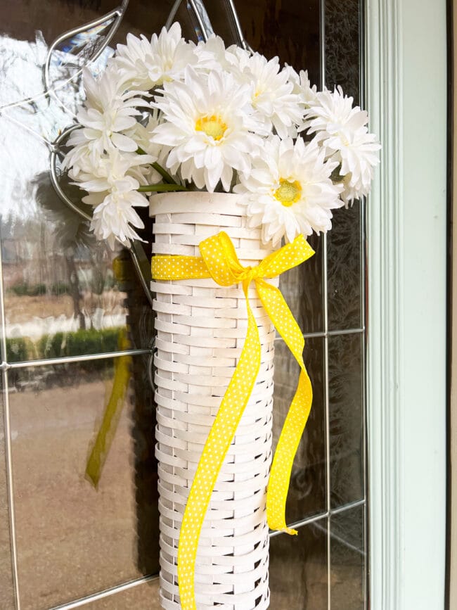 long white vintage basket hanging on door with white daisies and yellow bow