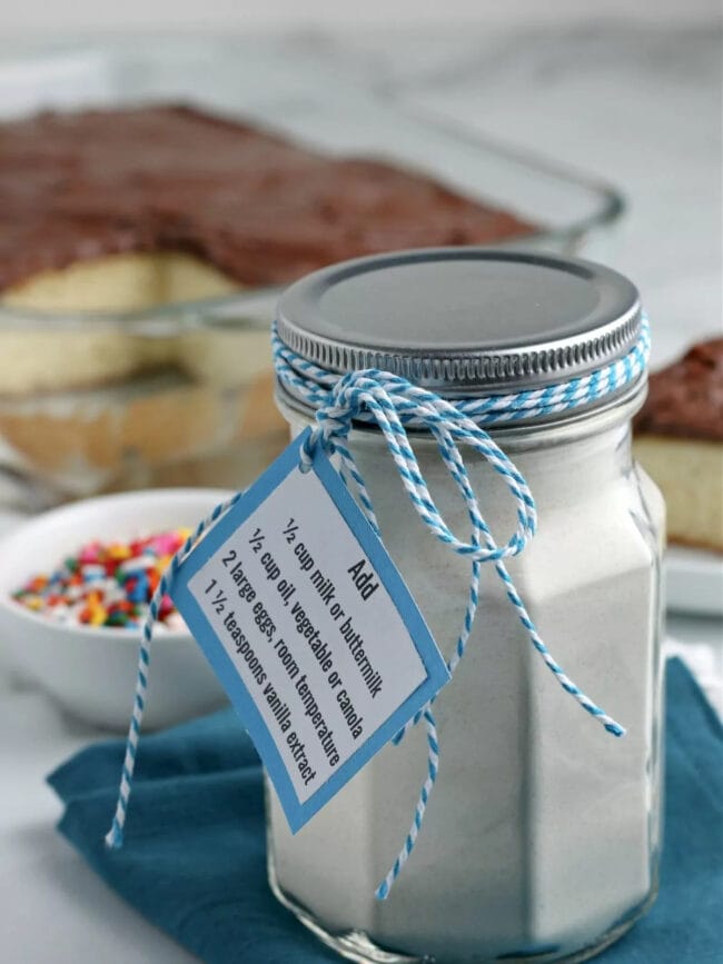 mason jar full of cake mix. Tied with blue and white string and a bowl of sprinkles in background