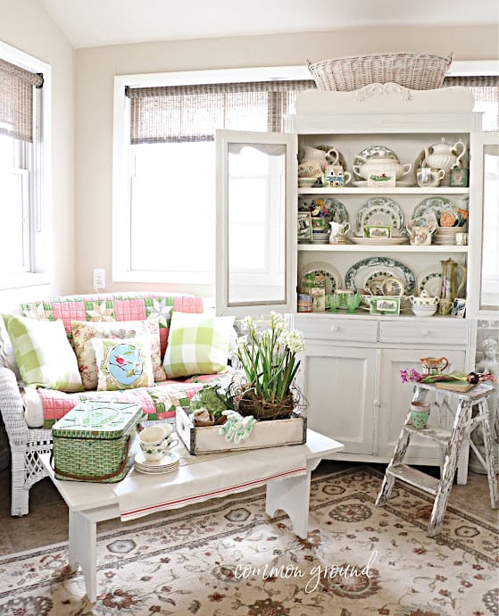 white sofa with pink and green pillows and quilt and a white hutch filled with green and white plates and spring decor