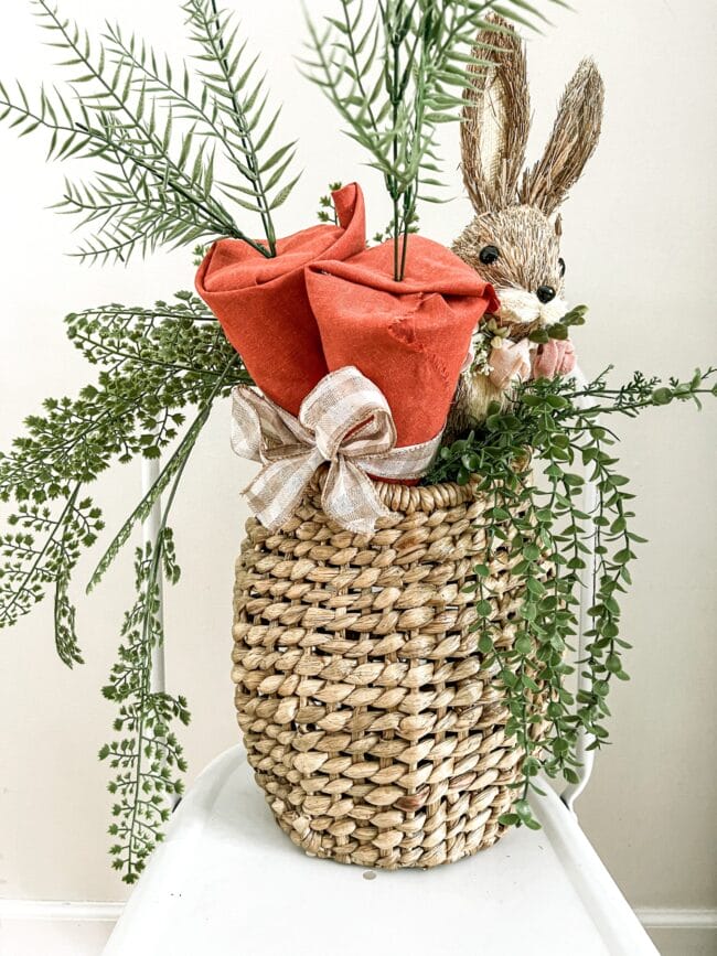 basket with large fabric carrots, a bunny and greenery hanging over the sides