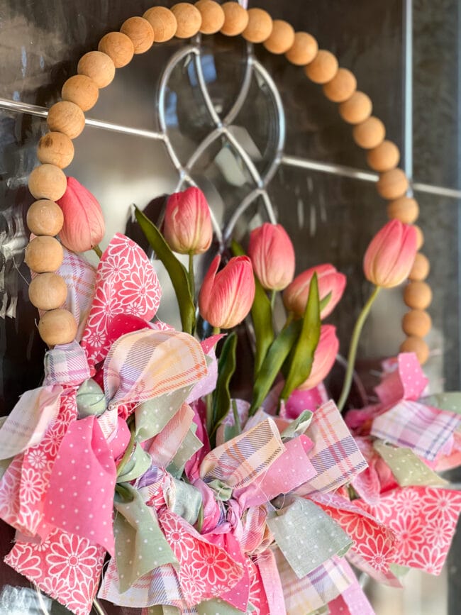 wood bead wreath hanging on glass door with fabric strips and faux tulips