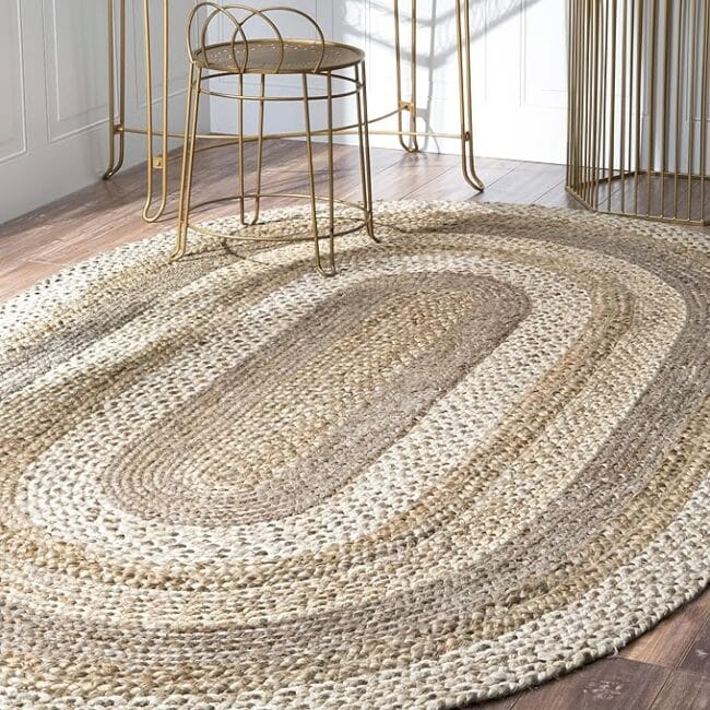 oval shaped neutral rug with brass stool sitting next to the edge