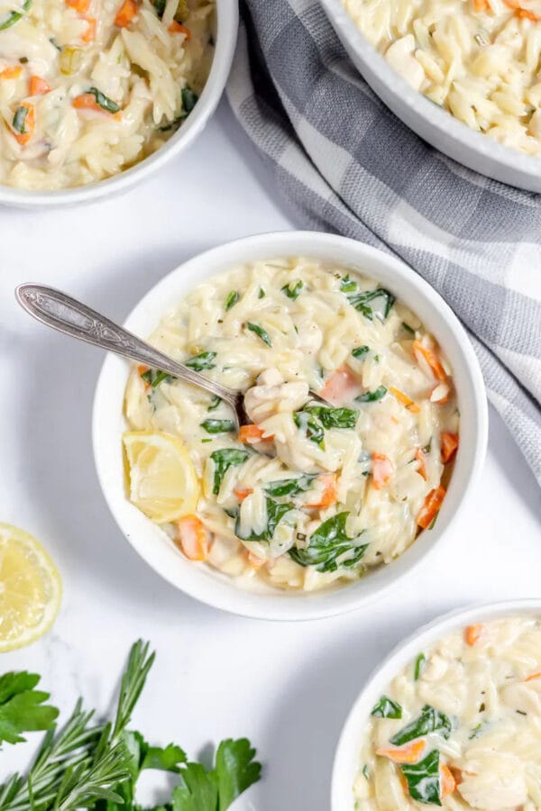 white bowl with orzo soup and a gray and white checked cloth sitting beside the bowl