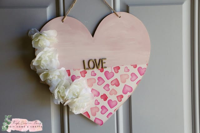 wooden heart with the word LOVE on it, white tissues flowers and small hearts painted across the bottom