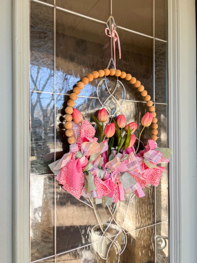 wood bead wreath with fabric strips and pink tulips on glass door