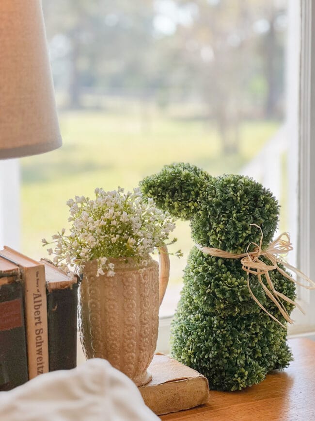 boxwood bunny with gold pitcher with faux white flowers and books in front of window