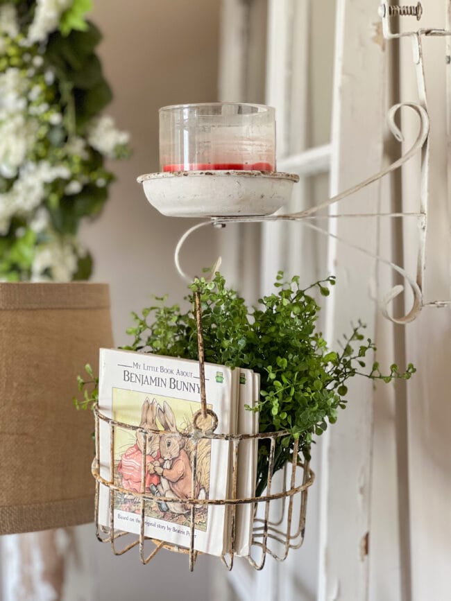 vintage candle holder with red candle and a metal basket hanging from bottom with greenery and bunny books