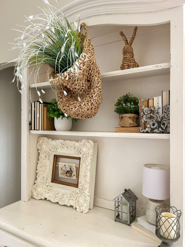 shelves with plant in hanging basket with faux green stems, bunnies and frame with bunny postcard and lamp