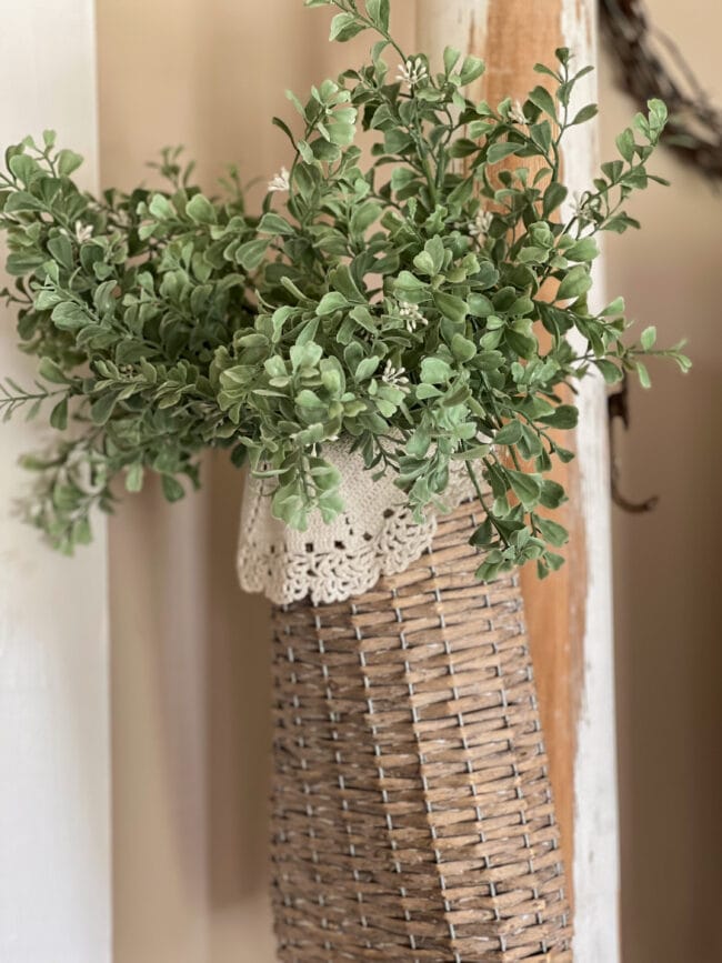 gray basket with a doily in front and faux green stems
