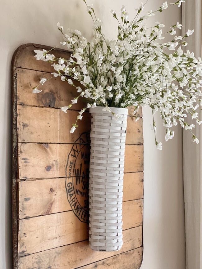 long white basket with white stems hanging on a vintage wood square piece