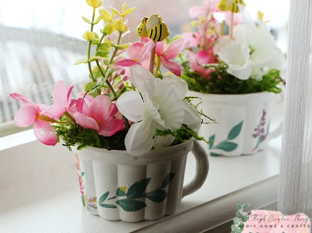 two crafted pots in window with flowers in pink, white and yellow