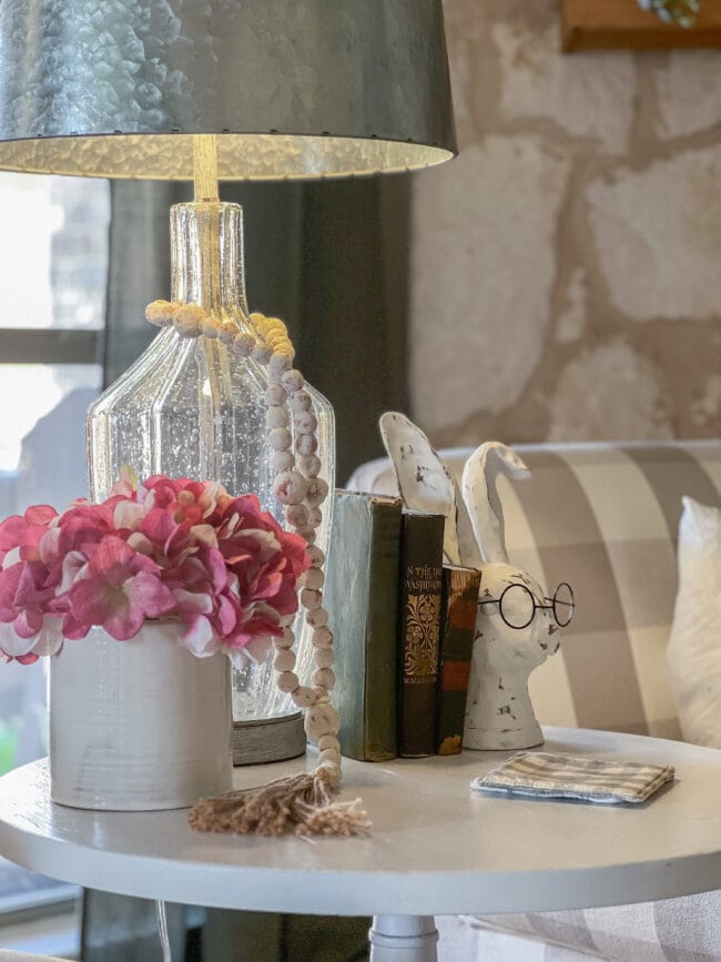 table with glass lamp, pink flowers and bunny head with glasses