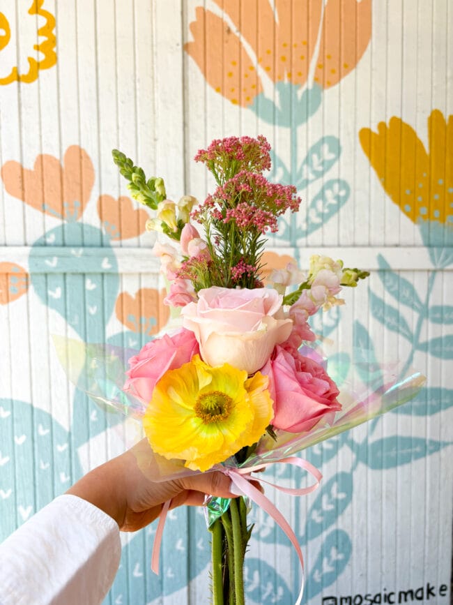 holding a floral bouquet of pink and yellow flowers