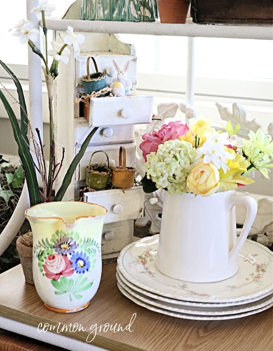 white pitcher with spring flowers, a small stacked chest of drawers with tiny baskets