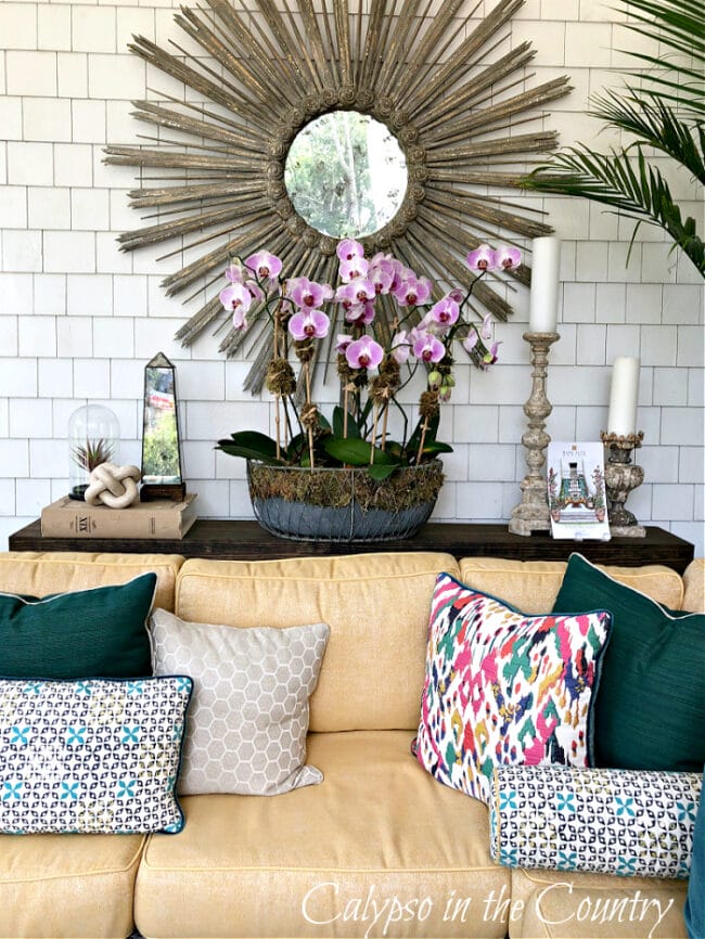 sofa table with medallion mirror, orchids and candles sitting in front of yellow sofa