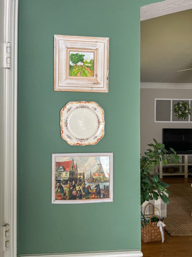 2 paintings with a small square plate hanging on a green wall
