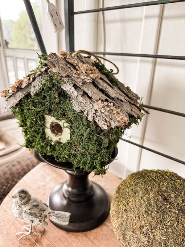 moss birdhouse with sticks for roof and a stone bird and moss ball