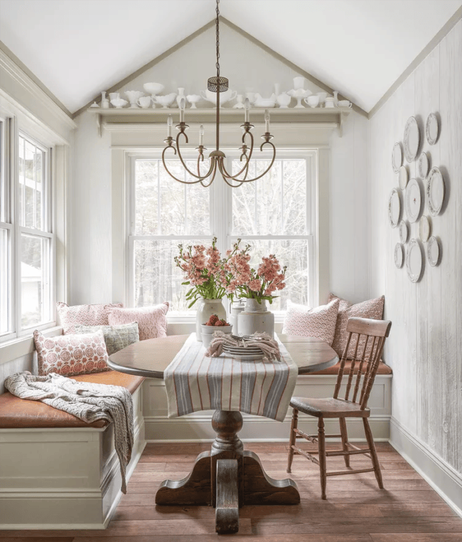 breakfast nook with bench, pink flowers, plates on wall and vintage chair