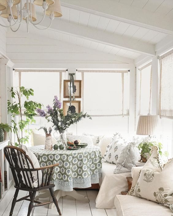 white sun room with round table and seating, flowers and lots of pillows