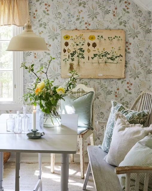 room with floral wallpaper, white table, yellow flowers and pillows on bench