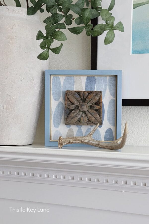 blue and white square art piece on mantel with antlers
