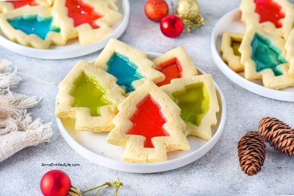 christmas tree shaped cookies on a plate filled with red, green and blue candy that looks like stained glass