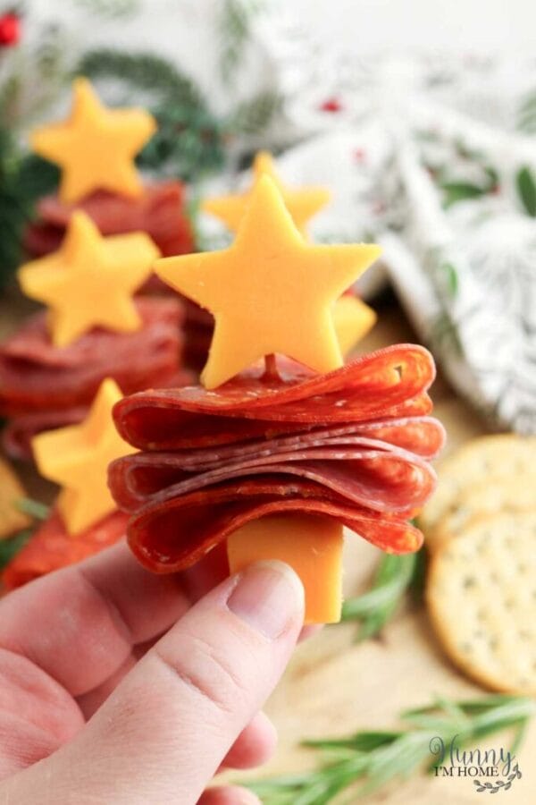 a hand holding a stack of folded pepperoni with a star shaped cheese cut out on top 