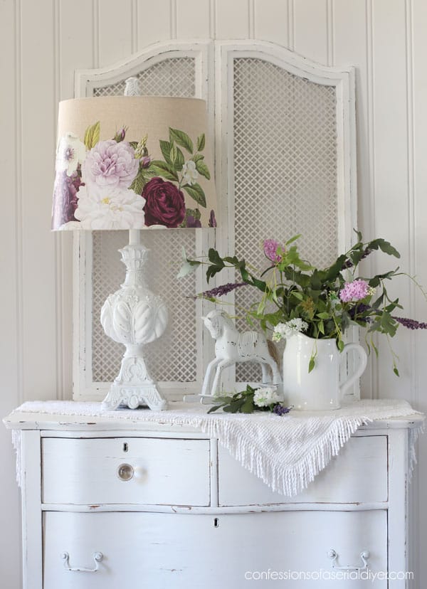 white lamp with a floral shade sitting on a white dresser with a plant