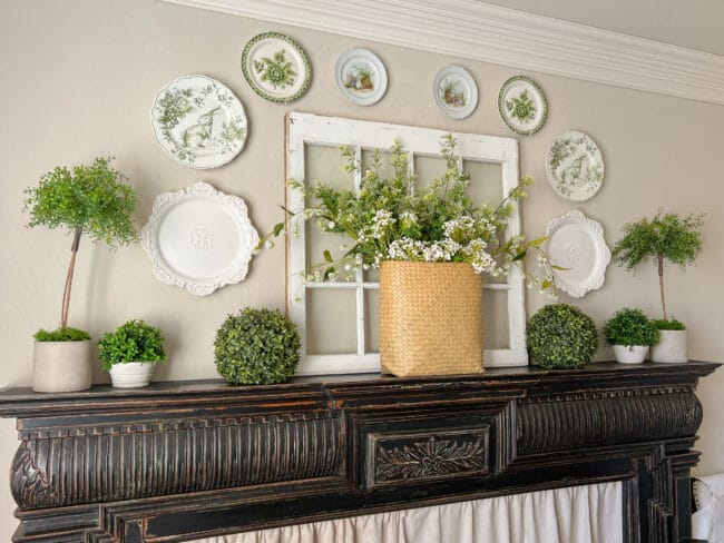 black mantel with basket of flowers sitting in front of antique window with plates hung on the wall