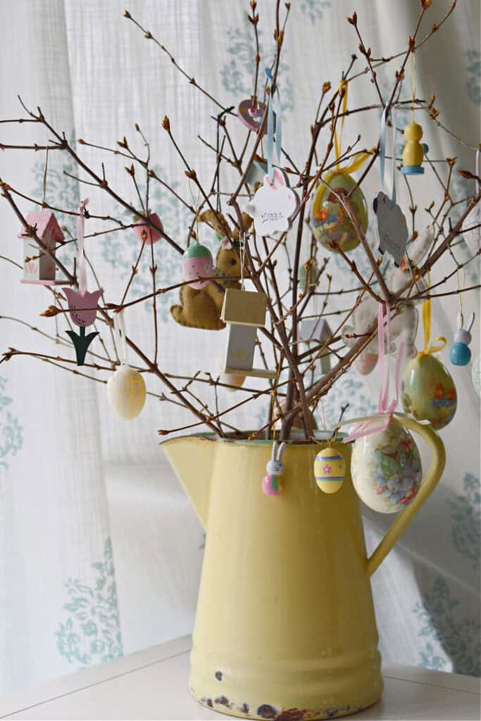 a yellow aluminum pitcher with eggs and bunnies hanging from the branches.
