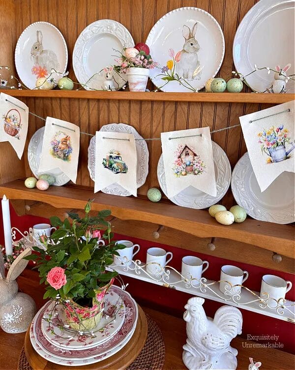 banner with bunnies hanging on a hutch decorated with plates and greenery