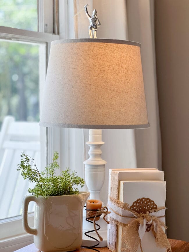 lamp with band majorette finial, old pitcher with faux greenery, stack of books and an old bed spring with a candle inside.