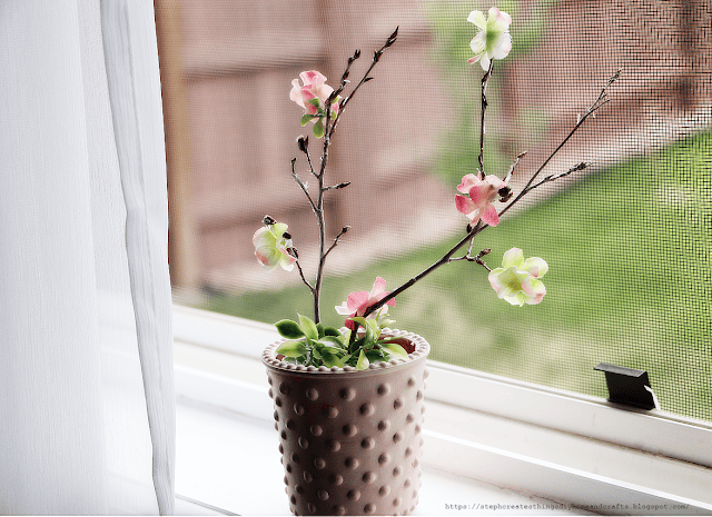 brown pot with a flowering branch sitting in window 