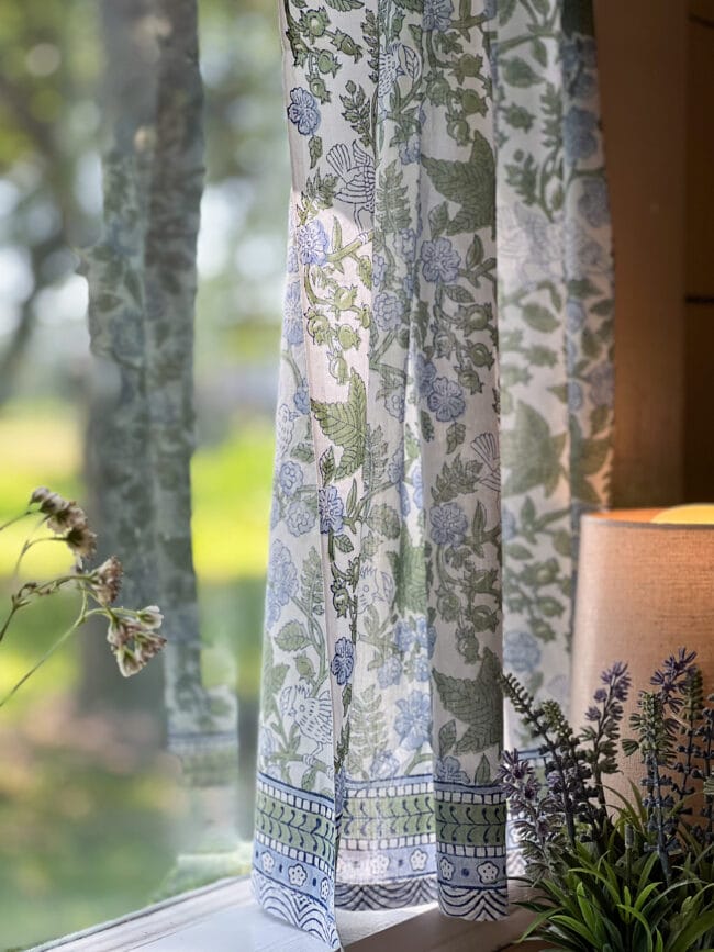 blue and green curtain on window with faux lavender plant and lamp in corner