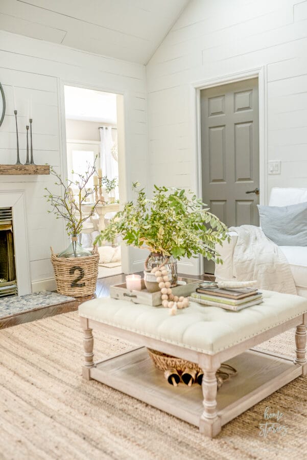 neutral room with an ottoman coffee table, green stems, coffee table books, beads and a candle