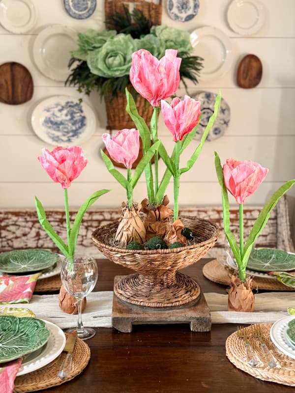 table setting with pink paper tulips inside a rattan pedestal bowl