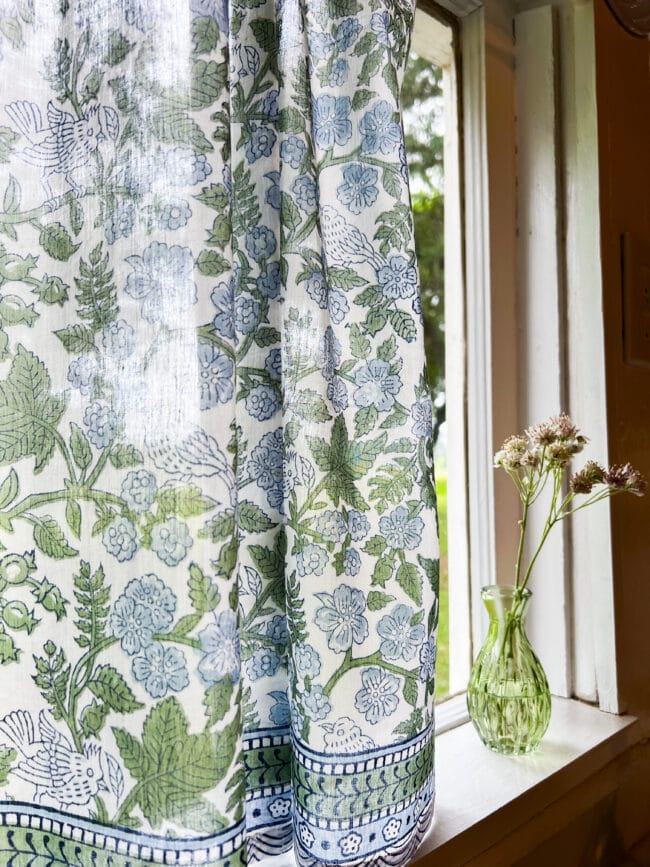 patterened blue and green sheer curtain and green vase of flowers