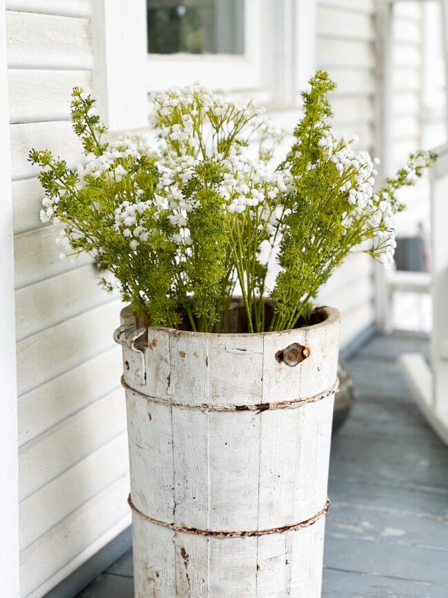 Vintage white ice cream bucket with faux flowers sitting on a porch