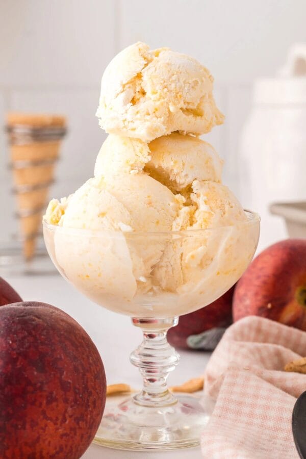 stacked homemade peach ice cream in a clear glass footed bowl
