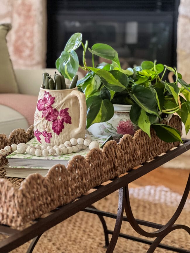 woven scalloped tray with a vintage pitcher holding candles, a string of beads and a plant