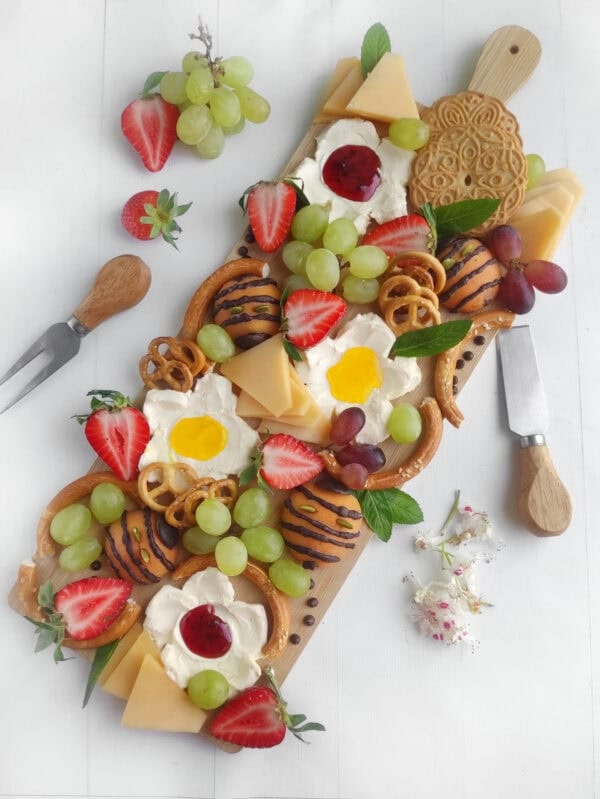 charcuterie board with flowers, bee shaped fruit, and pretzels