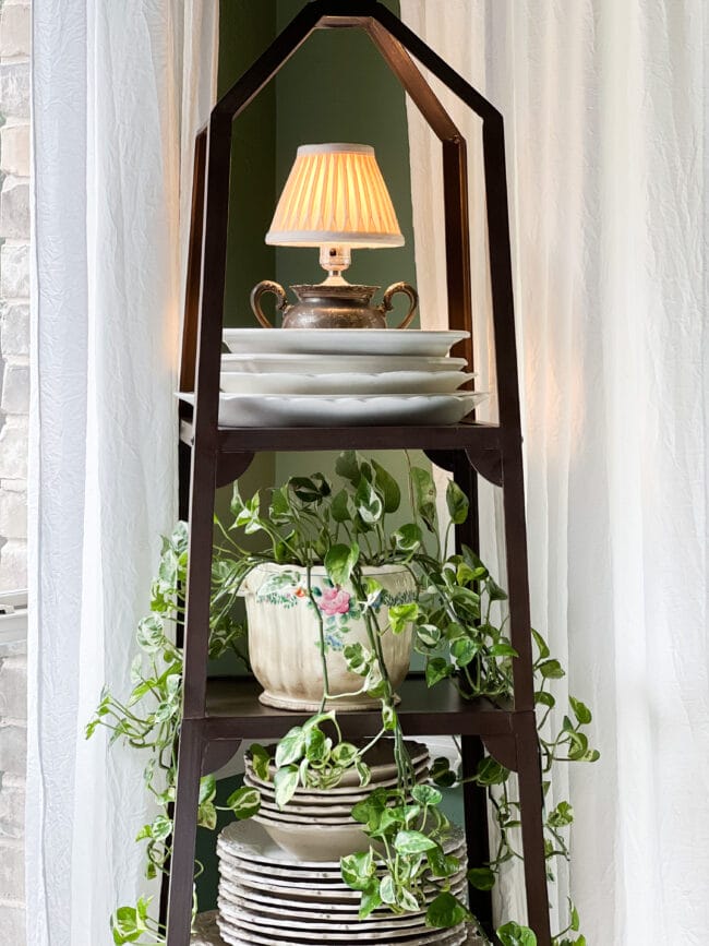 An etagere with a teapot lamp, plant and dishes