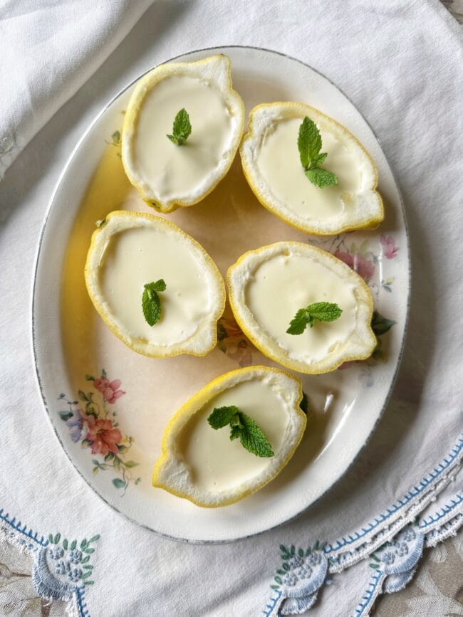 white oveal plate with five half lemons filled with dessert and a sprig of mint on each.
